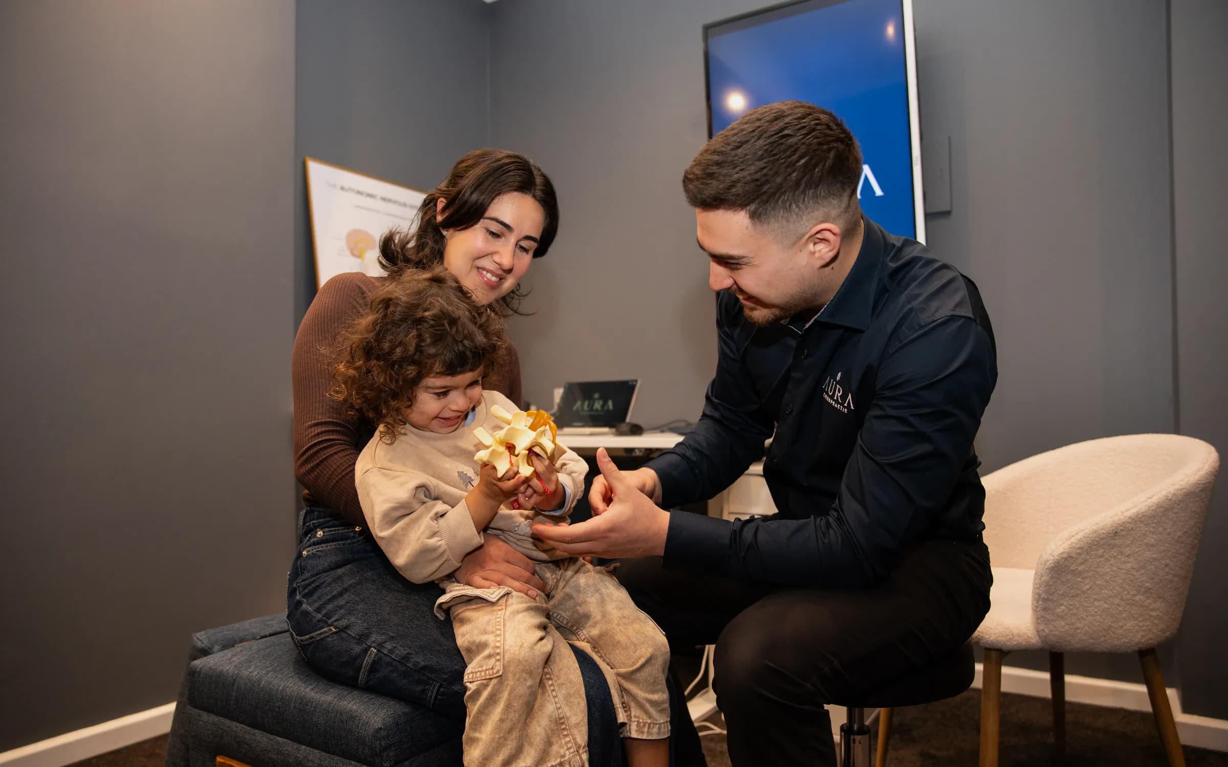 Dr Arthur Kaganovitch (Chiropractor) showing a spine model to a young family at Aura Chiropractic in Toorak
